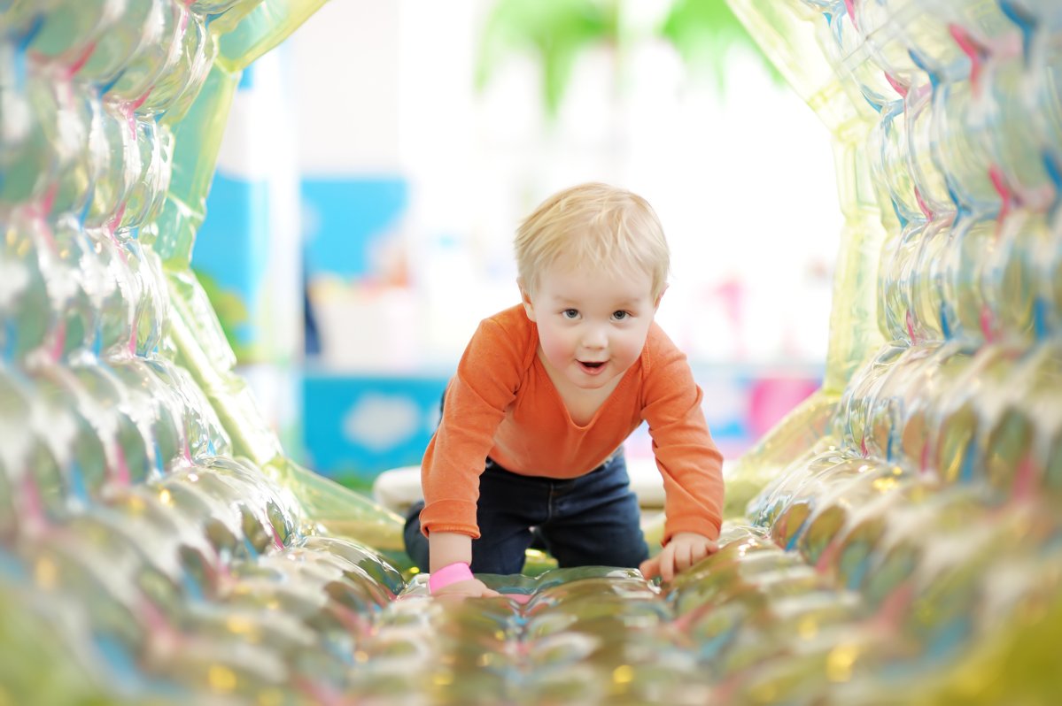 Active toddler boy having fun on inflatable attraction in entertaining center. Funny child is playing on indoor playground. Kids amusement park.