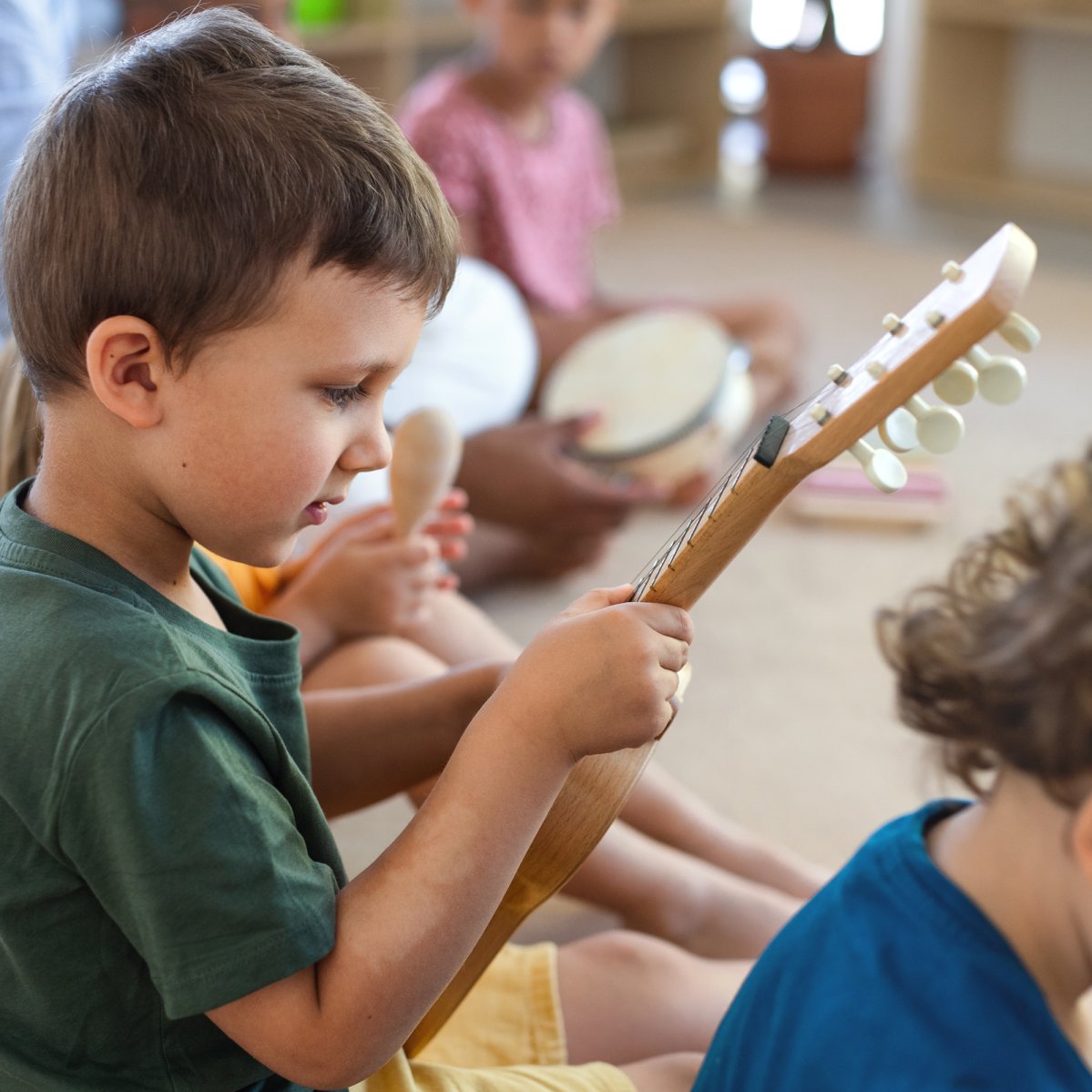 Group of small nursery school children sitting on floor indoors in classroom, playing musical instruments.