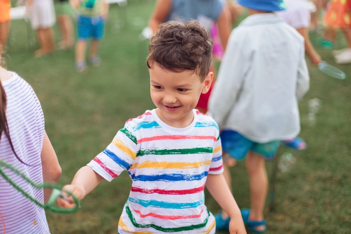 the child inflates large soap bubbles. Street animation program, happy child on a green lawn. Summer vacation. A boy in bright striped clothes with soap bubbles. Large portrait, horizontal.